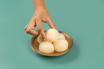 Traditional Indian Rasgulla Mithai in a Brass bowl being picked up by a hand to eat