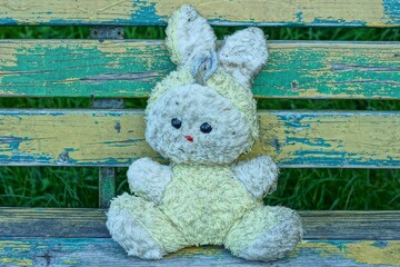 one soft plush gray with ears dirty toy children's funny with black eyes and red nose and yellow body hare lies on a wooden bench