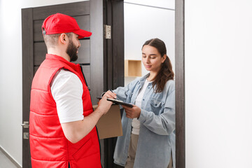 Courier with box and receiver signing for delivered parcel indoors