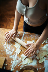Woman with big breast rolling out homemade dough on a rustic wooden table, surrounded by flour and pastry pieces. Perfect for cooking blogs, recipe sites, and kitchen lifestyle ads. 