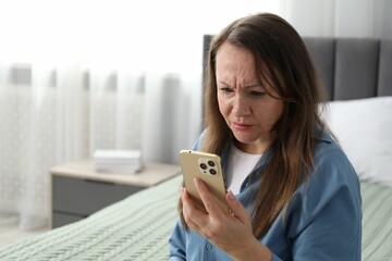 Woman with vision problem using smartphone on bed at home, space for text