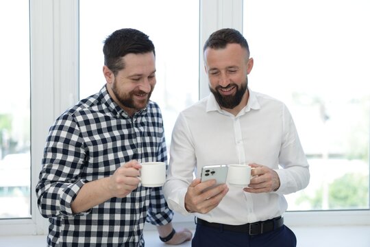 Colleagues with coffee and smartphone during lunch break in office