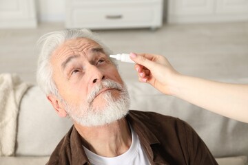 Woman dripping medication into man's eye at home, closeup
