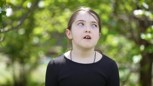 Teen Girl Shows Boredom as She Puffs Her Cheeks and Blows Air in Green Outdoor Setting During Daytime. Little cute teenage female outdoor, kid expression. Children on nature background