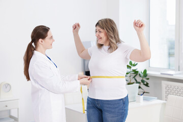 Fototapeta premium Weight loss. Nutritionist measuring happy overweight woman's waist with tape in clinic