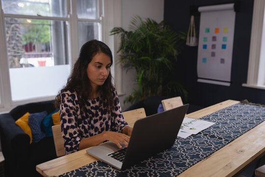 Laptop displaying chart data and documents lying on wooden table with blue runner near potted plant
