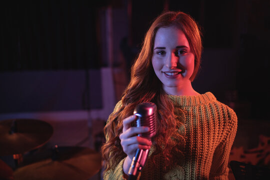 Singer gripping vintage microphone and performing on stage with drum kit under red blue lights
