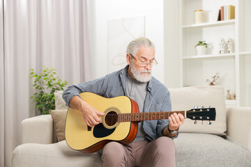 Relaxing hobby. Senior man playing guitar on sofa at home