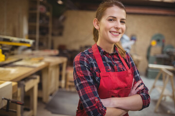 Woman carpenter standing wearing red apron arms crossed in workshop with miter saw, copy space