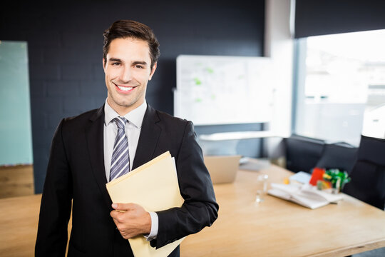 Manila file folders sitting on table with papers, laptop and glass of water in boardroom