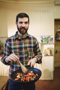 Black frying pan is sizzling mushrooms and red bell pepper on wooden countertop near ceramic jugs