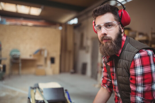 Table saw cutting wooden board on workbench in woodworking shop, with scattered lumber and skylight