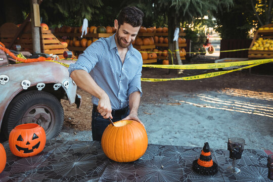 Male carving pumpkin top with knife at outdoor stall with skull decals and caution tape
