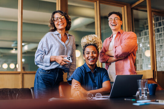 Smiling coworkers gathered around a laptop in a casual office setting