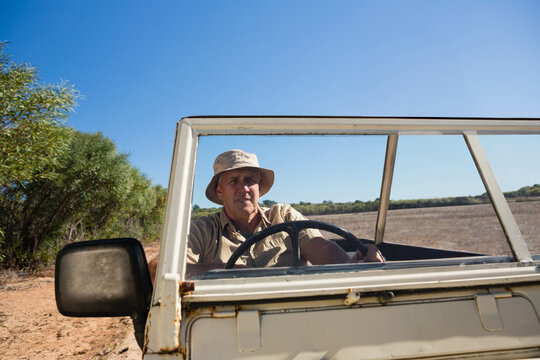 Man sitting at steering wheel of white 4x4 on outback track wearing beige bucket hat