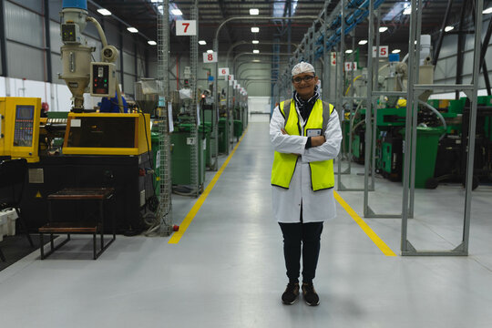 Female technician wearing safety vest and ID badge inspecting machines in factory hall