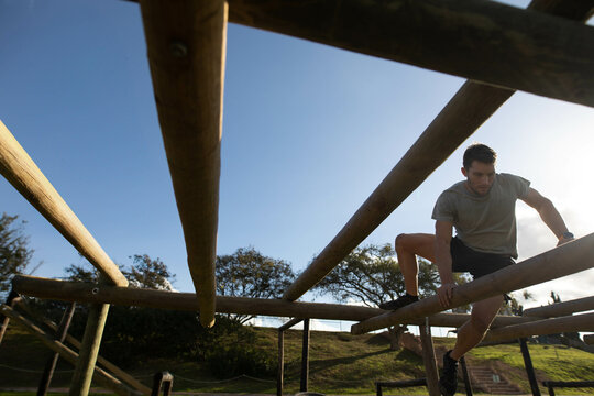 Man in his 20s climbing wooden beams on grassy park trail with wristwatch, copy space