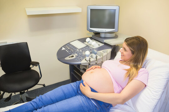 Pregnant woman lying on examination table at prenatal clinic, using ultrasound console, copy space