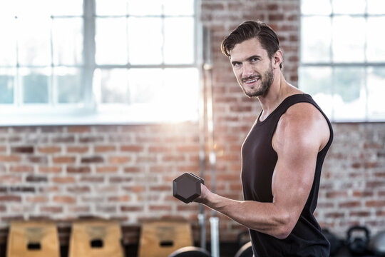 Man lifting hexagonal dumbbell in fitness studio with wooden boxes, weight plates, copy space
