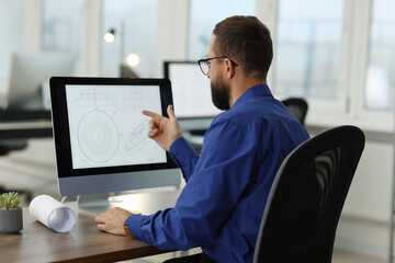 Technician making digital engineering drawing on computer at desk in office, back view