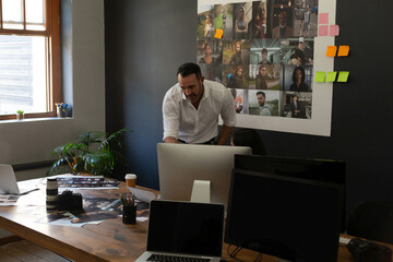 Man leaning over desk at creative workspace, examining printed pictures by camera and monitor