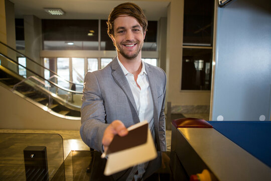 Male traveler wearing suit extending passport and boarding pass at airport check-in counter