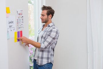 Man pointing to colored notes by Creative Idea poster, thumbnails beside curtained window in studio