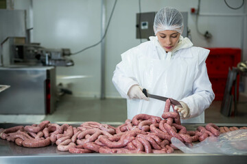 Female meat processing worker slicing sausage links at stainless steel table in processing facility