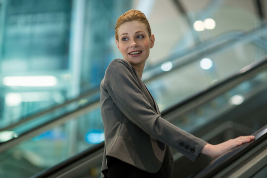 Female businesswoman standing on escalator in airport terminal, gripping glass-and-steel handrail