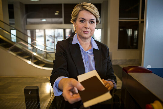 Senior woman wearing business attire handing passport to scanner at airport checkpoint counter