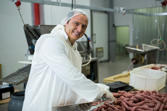 Male meat processing worker linking sausages on metal table at plant using linking tool, copy space