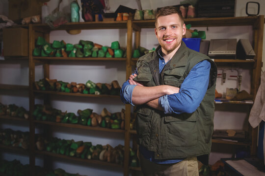 Man smiling while standing in cobbler workshop organizing wooden shoe lasts on shelves, copy space