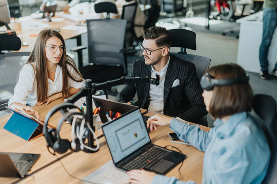 A diverse group of employees engaged in a business meeting around laptops and tablets in a modern office. The dynamic interaction emphasizes teamwork and communication in a multicultural work setting.