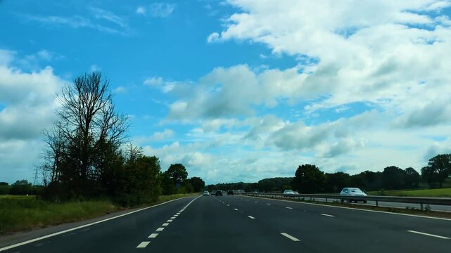 POV Car Dashcam on Slip Road Entering M5 Motorway in South West England with Bright Blue Sky with Trees and Other Transportation Vehicles including Cars and Trucks.