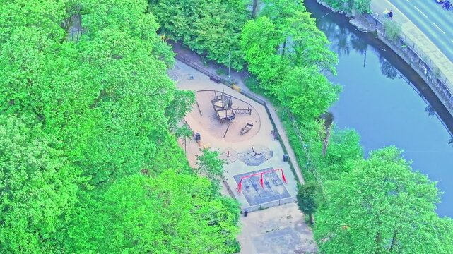 Drone shot over riverside playground in Matlock Bath, Derbyshire, by Derwent river, with climbing structures and swings, surrounded by trees viewed from above, lush foliage, aerial static