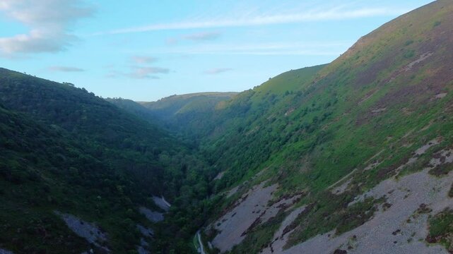 Pushing Drone View Along Valley at Sunrise in Summer Along Exmoor Coast Path with Dense Green Forest. Example of Beautiful British Countryside Viewed from the Air. Bird's Eye View.