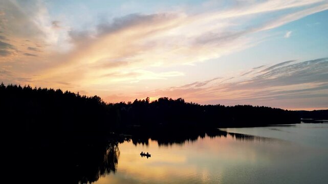 Silhouetted canoe with people fishing on a calm Norwegian lake during a vibrant sunset