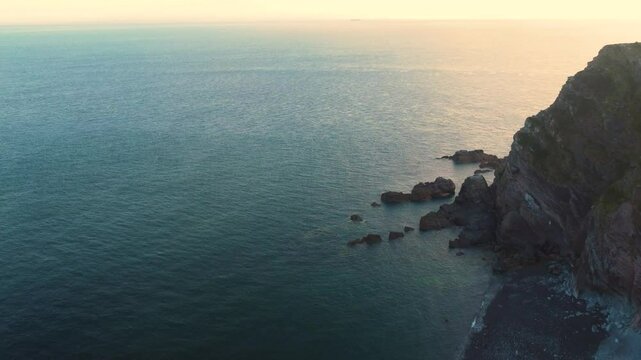 Establishing Shot of English Pebble Rocky Beach with Calm Ocean and Sun Reflecting on Sea Surface. Filmed in North Devon near Coast Salt Path.