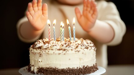 A child prepares to blow out candles on a birthday cake with chocolate sprinkles and white frosting.