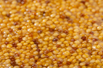 French Dijon mustard in a metal spoon, top view on mustard grains background. Gastronomy concept, organic food. Sauce. Slow rotation in a circle.	