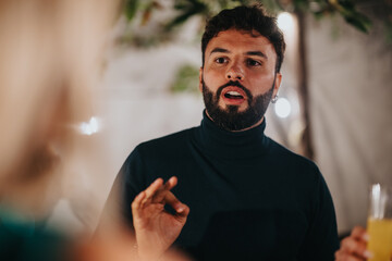 A casually dressed man with a beard communicates energetically during an outdoor gathering.