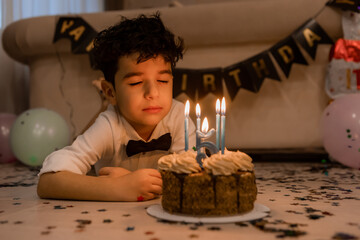 little boy makes a wish and blows out the candles on his birthday cake
