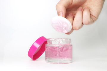 make up container with pink lid and white between the lid and a pink gel product or cream and a hand showing the product
