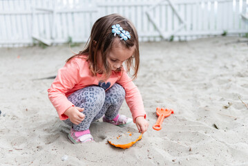 Little girl playing with sand mold and rake in sandbox