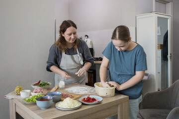 Portrait of child girl daughter and mother preparing dough for pizza and smiling while baking in kitchen at home, family together
