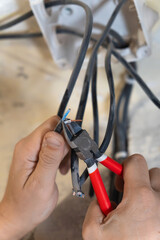 Electrician uses pliers to meticulously cut and prepare electrical wires, performing essential maintenance work on a residential electrical system. Vertical photo