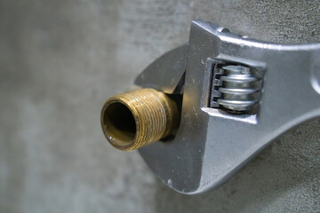 Adjustable wrench gripping a brass pipe fitting during plumbing work, showcasing the tools and materials used in plumbing and home repair