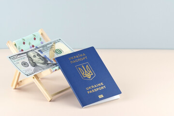 Ukraine passport and chaise lounge with dollars and globe on a light background.