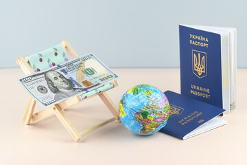Ukraine passport and chaise lounge with dollars and globe on a light background.