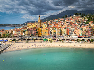Colorful old town of Menton on the French Riviera, with pastel facades, baroque basilica, and beach under dramatic skies